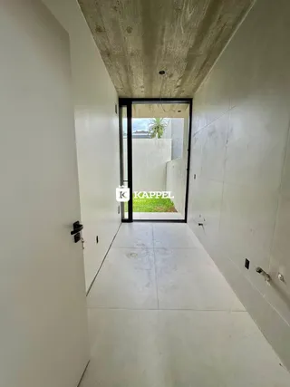 Corredor interno com paredes brancas e piso claro, com vista para o exterior.