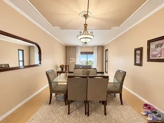 Sala de jantar com mesa de vidro e cadeiras estofadas.