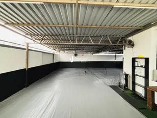 Espaço interno industrial com teto de estrutura metálica e piso coberto por lona cinza.