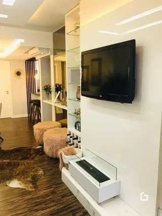 Sala de estar com piso de madeira e televisão montada na parede.