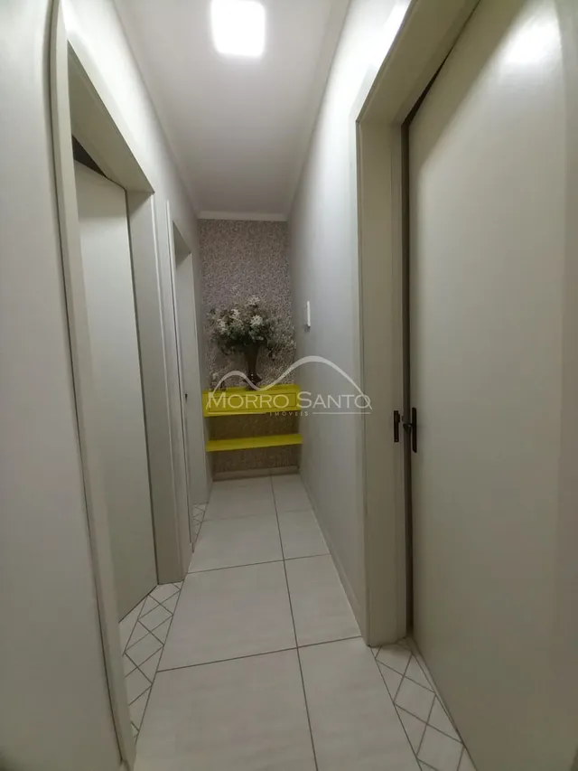 Foto de um corredor interno com paredes brancas e piso de azulejo claro.