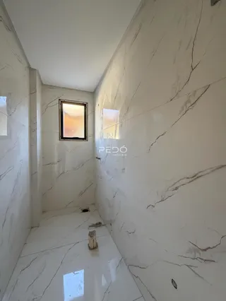 Corredor interno com paredes de mármore branco e piso claro.
