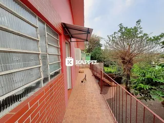 Vista externa de uma edificação vermelha com um caminho pavimentado e vegetação ao lado.