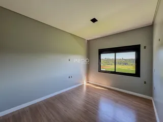 Ambiente interno de uma sala com piso de madeira clara e grande janela com vista para a paisagem.