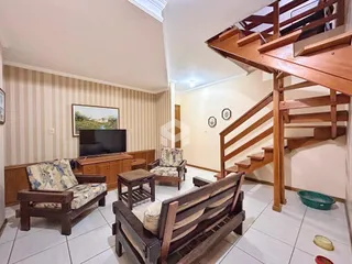 Sala de estar com móveis de madeira e escadaria no interior de uma residência.