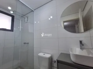 Banheiro com revestimento cerâmico e box de vidro.
