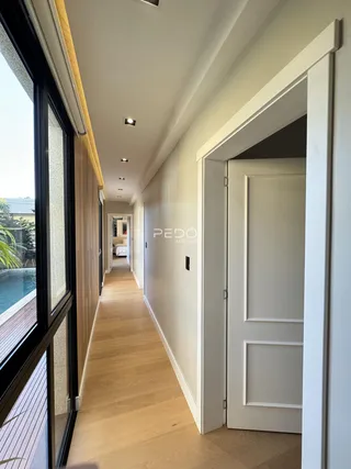 Corredor interno de uma residência com piso de madeira clara e paredes brancas.