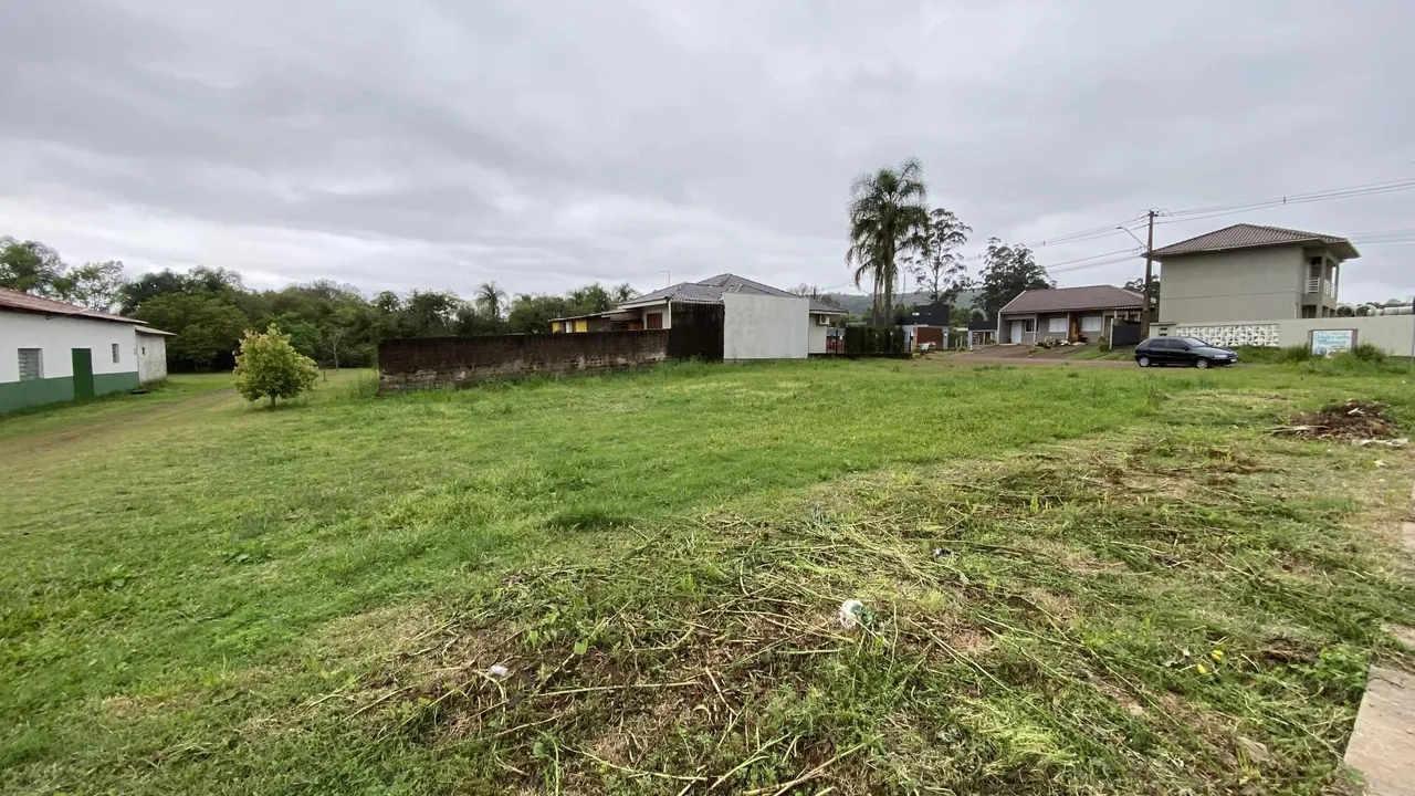 Vista externa de um terreno gramado com construções residenciais ao fundo.