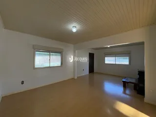 Ambiente interno de uma sala ampla com piso de madeira clara e paredes brancas.