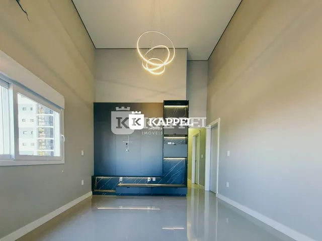 Uma sala ampla com pé direito alto e uma área de cozinha planejada escura.