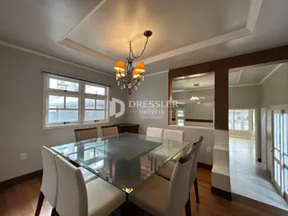 Uma sala de jantar com mesa de vidro e cadeiras brancas.