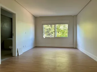 Sala com piso de madeira e grande janela iluminada.
