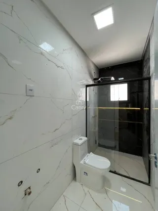 Banheiro com revestimento de mármore branco e box de vidro transparente.