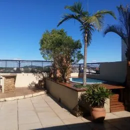 Vista externa de um terraço com piso de cerâmica e vegetação.