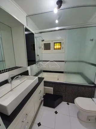 Foto de um banheiro com revestimento de azulejos escuros e bancada branca.