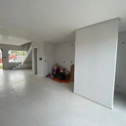 Ambiente interno amplo com piso claro e escadaria visível no fundo.