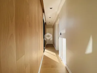 Um corredor interno com piso de madeira clara e paredes claras.