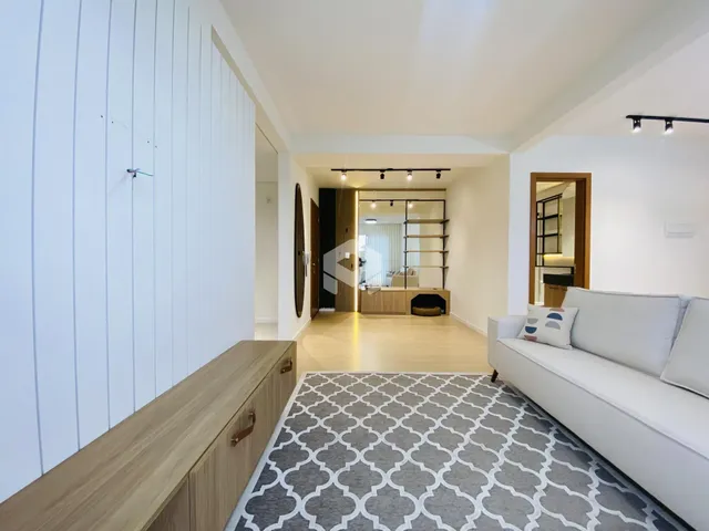 Sala de estar com piso de madeira clara e sofá branco.