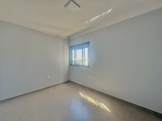 Ambiente interno de uma sala ampla com paredes brancas e piso claro.