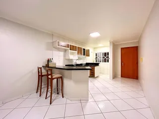 Vista interna de uma cozinha com armários brancos e piso de cerâmica clara.
