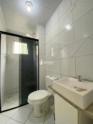 Interior de um banheiro com revestimento cerâmico branco e box de vidro.