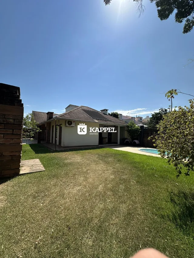 Fachada de uma residência com jardim e piscina sob um céu azul claro.