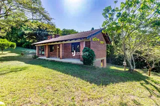 Casa de tijolos vermelhos em terreno gramado com vegetação densa.