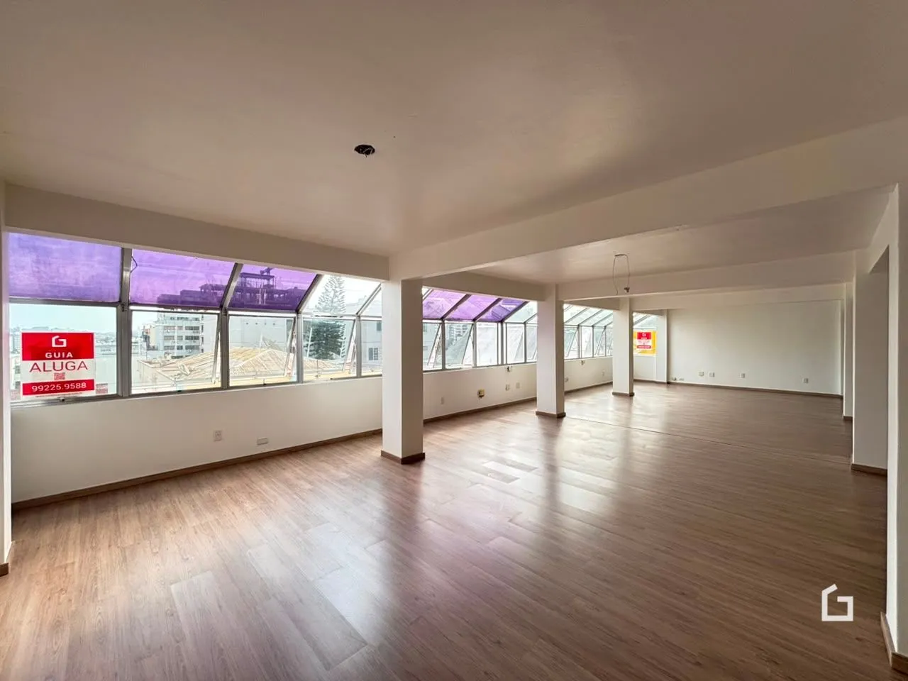 Um espaço amplo com piso de madeira e grandes janelas.