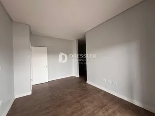 Interior de uma sala com piso de madeira e paredes brancas.
