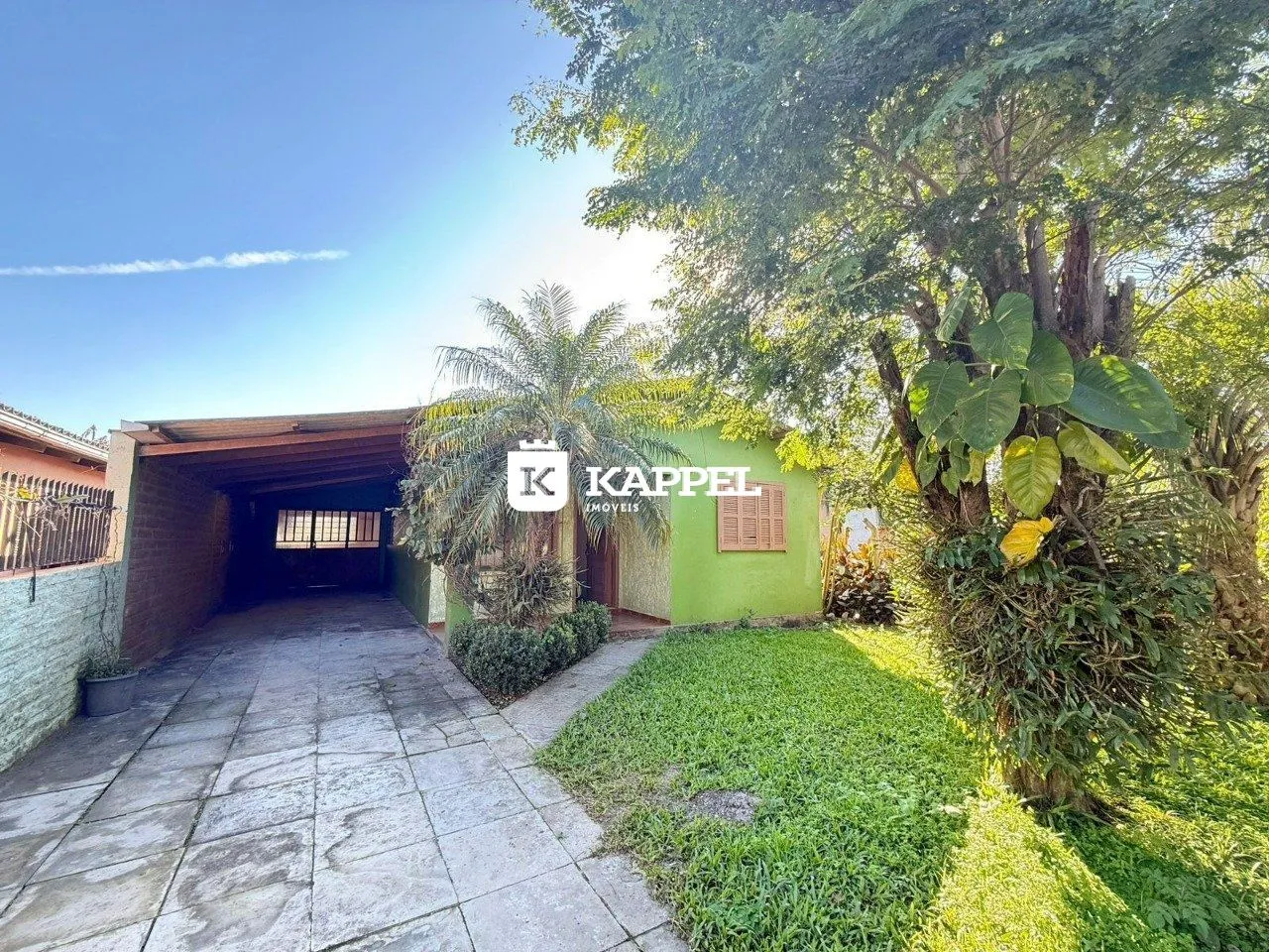 Foto da fachada de uma casa verde com um pátio pavimentado.