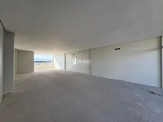 Imagem de um espaço interno vazio com paredes brancas e piso de concreto.