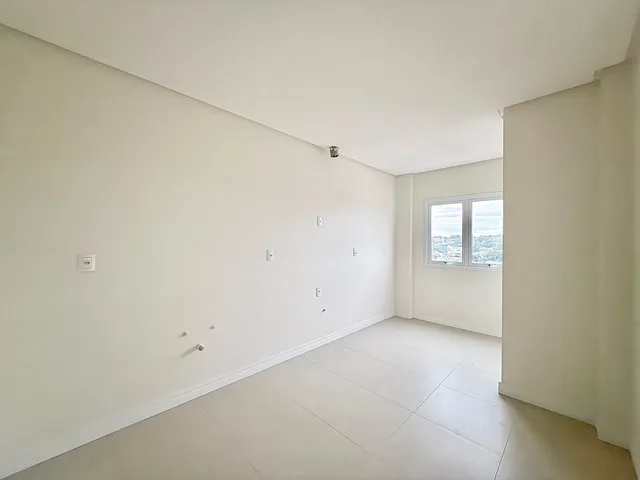 Sala de estar ampla com paredes brancas e piso claro, mostrando o interior de um imóvel.