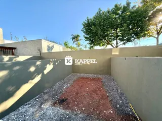 Vista externa de um terreno com cascalho e terra, delimitado por um muro alto.