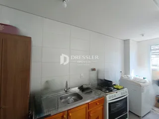 Vista interna de uma cozinha com revestimento branco e armários de madeira.