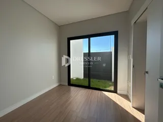 Vista interna de uma sala com piso de madeira e porta de vidro para o quintal.