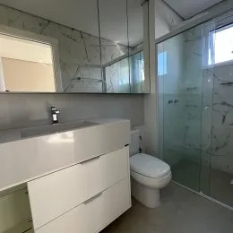 Foto de um banheiro com bancada branca e box de vidro transparente.