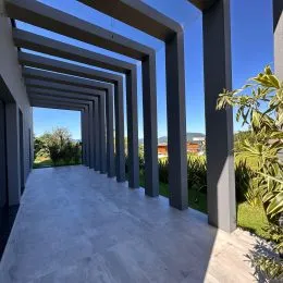 Vista de uma estrutura arquitetônica externa com colunas e vigas em um pátio.