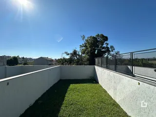 Vista externa de um quintal com muro branco e gramado verde.