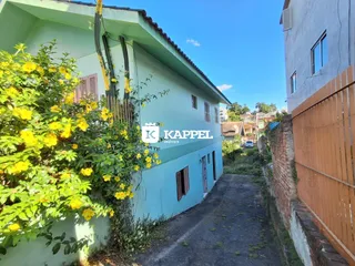 Fachada de uma casa azul com vegetação exuberante ao lado de um caminho de acesso.