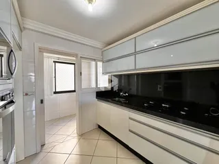 Vista interna de uma cozinha com armários brancos e bancada escura.