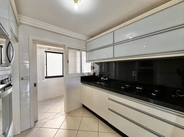 Vista interna de uma cozinha com armários brancos e bancada escura.