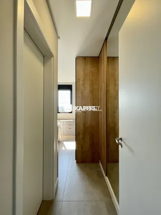 Hall de entrada com paredes brancas e porta de madeira no interior de uma residência.
