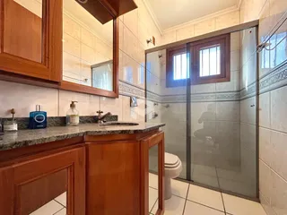 Interior de um banheiro com box de vidro e armários de madeira.
