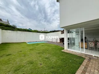 Vista externa da propriedade mostrando um gramado extenso e uma piscina.