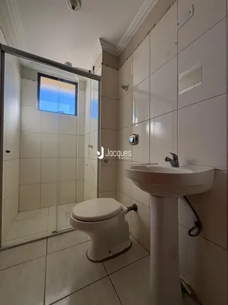 Interior de um banheiro com azulejos brancos e box de vidro.