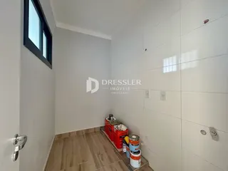 Vista interna de um corredor com paredes brancas e piso de madeira clara.