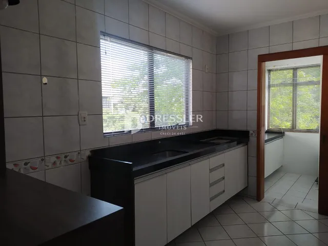 Vista interna de uma cozinha com revestimento de azulejos cinzas e armários brancos.