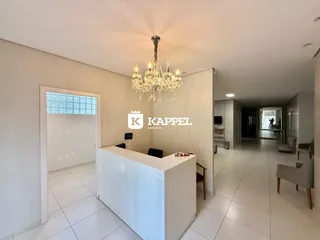 Vista do hall de entrada com balcão branco e lustre de cristal.