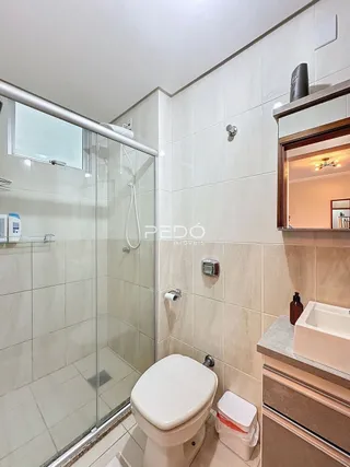 A foto mostra o interior de um banheiro com box de vidro e vaso sanitário.