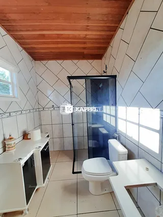 Foto do interior de um banheiro com revestimento de azulejos brancos e teto de madeira.